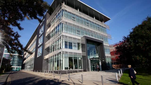 Modern glass-fronted building with a sleek design, surrounded by greenery and a clear blue sky.