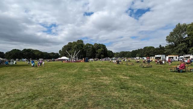 Wide view of a grassy field filled with people, tents, and food stalls under a partly cloudy sky.