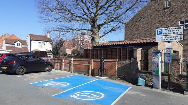 East Parade Car Park with marked disabled spaces, payment machine, and a large tree nearby, set against residential buildings.