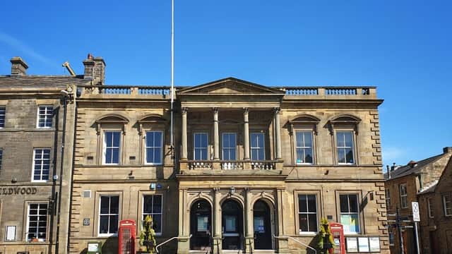 Skipton Town Hall features classical architecture, a Union Jack flag, and flower planters in a sunny square.