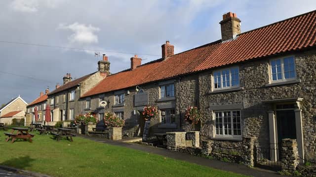 Charming stone building with a red-tiled roof, flower baskets, and picnic tables outside in a quaint village setting.