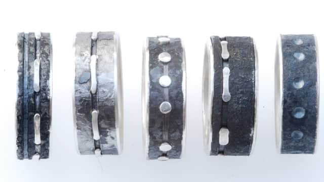 Five unique metal rings with textured surfaces and varying designs, displayed against a white background.