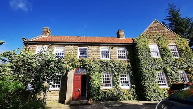 Stone building covered in ivy, featuring a red door and large windows, set against a bright blue sky.
