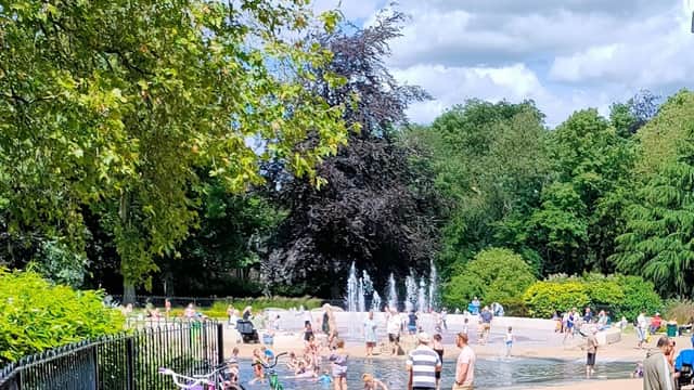 Families enjoying a sunny day at Clifton Park, with a splash pad, greenery, and bicycles nearby.