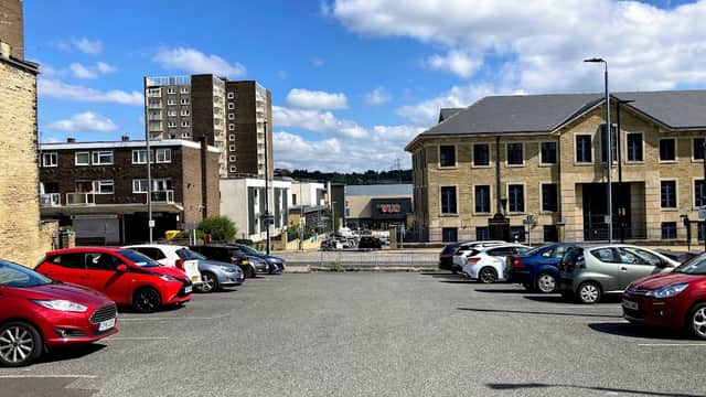 Free parking area with various cars, buildings in the background, and a clear blue sky with clouds.