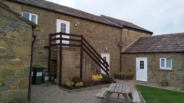 Stone cottages with a wooden staircase, picnic table, and garden in a rural setting.