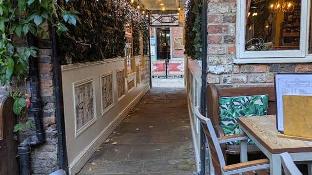 Charming stone pathway leading to a cozy restaurant with greenery and warm lighting, inviting outdoor seating.