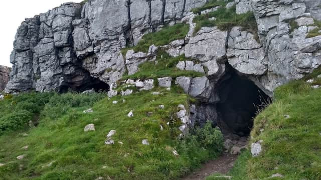 Rocky cave entrance surrounded by lush green grass and rugged terrain in Langcliffe, Yorkshire.
