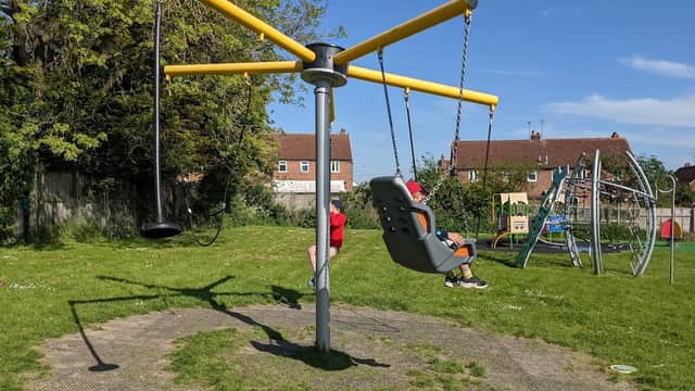 Bright playground with a large yellow swing set, green grass, and play equipment in the background under a clear blue sky.