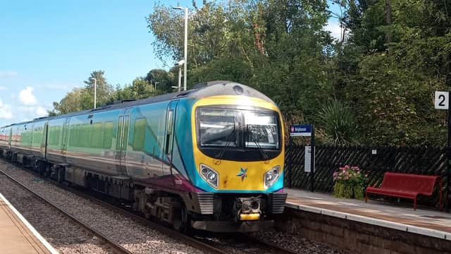 A colorful train at Brighouse station, with greenery and a red bench visible on the platform.