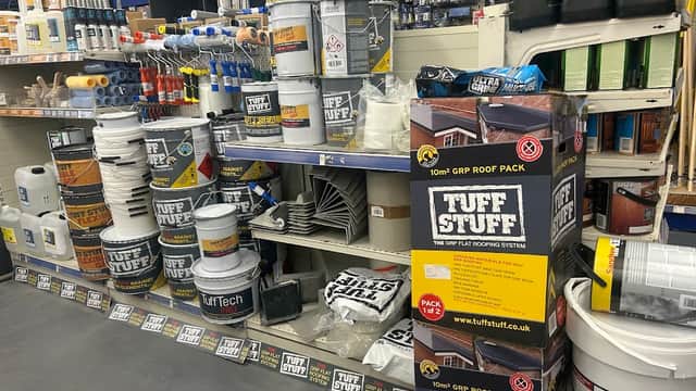 Ironmongers display featuring buckets, tools, roofing materials, and various home improvement supplies on shelves.