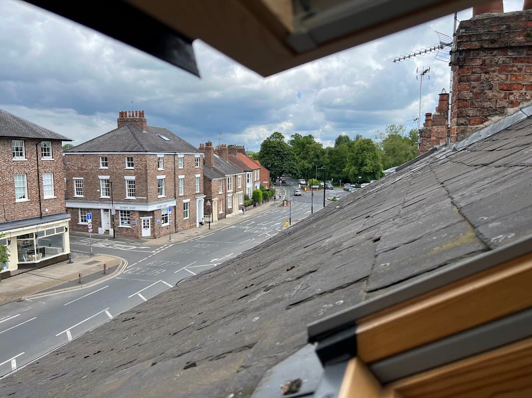 View from a roof window showing brick buildings, a street, and greenery in York, Yorkshire under a cloudy sky.