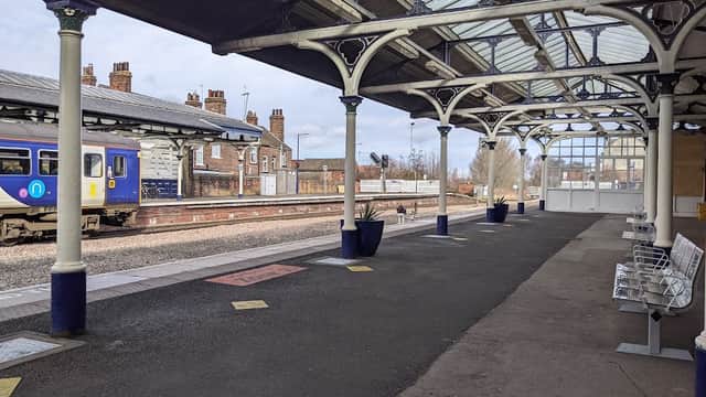 Railway platform at Selby Station with benches, planters, and a train approaching in the background.