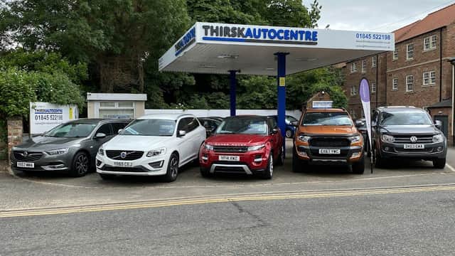 Thirsk Autocentre with a lineup of six vehicles under a canopy, surrounded by greenery and buildings in Thirsk, Yorkshire.