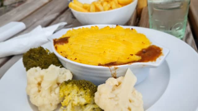 Shepherd's pie with a golden topping, served with cauliflower and broccoli, alongside a bowl of fries.