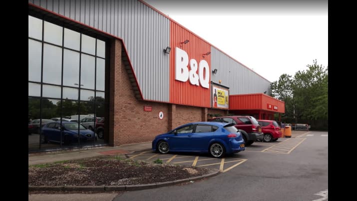 B&Q store exterior with parking area, featuring a blue car and several others, surrounded by greenery in Bridlington.