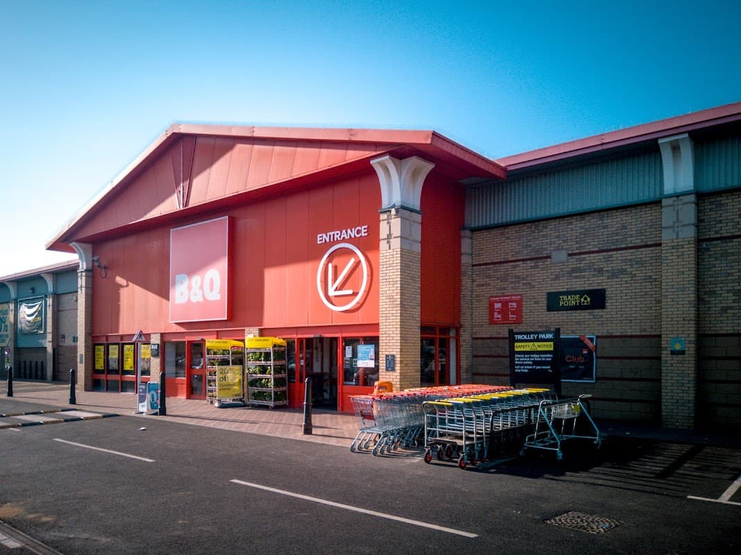 Brightly colored B&Q store entrance with shopping carts lined up outside, clear blue sky overhead.