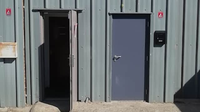 Gray metal building with a sign for "Topcliffe Motorbikes" above a main entrance and a smaller door to the side.