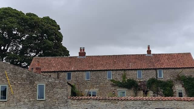 Stone cottages with red roofs, lush green lawn, and a large tree under a cloudy sky in Sproxton, North Yorkshire.