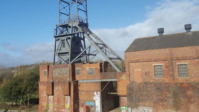 Old brick industrial building with a tall coal mine tower, surrounded by greenery under a blue sky.