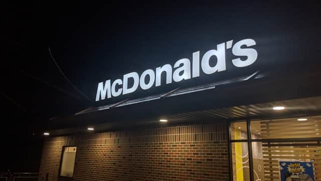 McDonald's sign illuminated at night, with brick facade and large windows showcasing the cafe's interior.
