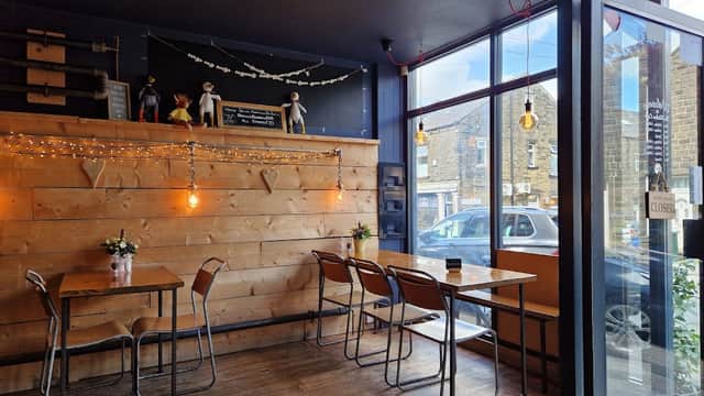 Cozy café with wooden walls, tables, chairs, and decorative string lights; large windows showcasing the street outside.