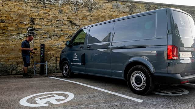 Electric vehicle charging station with a gray van parked beside it in Coneysthorpe, Yorkshire, against a stone wall.