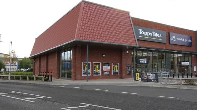 Brick building with a red tiled roof, large windows, and signage for Topps Tiles and HSL. Parking area visible.