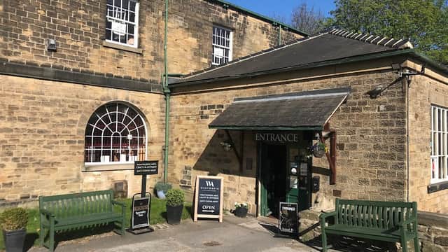 Stone building with green accents, entrance sign, and benches outside, surrounded by trees in Wentworth, Yorkshire.