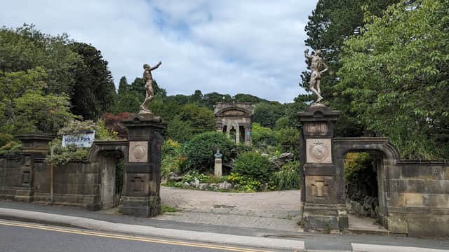 Entrance to Holden Park featuring stone gates, statues, and lush greenery under a cloudy sky.
