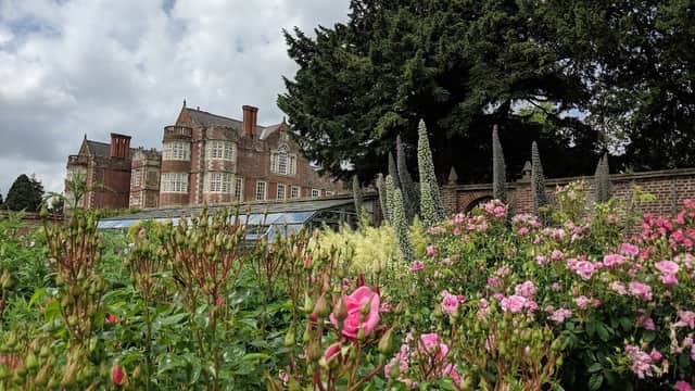 Burton Agnes Hall with lush gardens and blooming flowers in the foreground, under a partly cloudy sky.