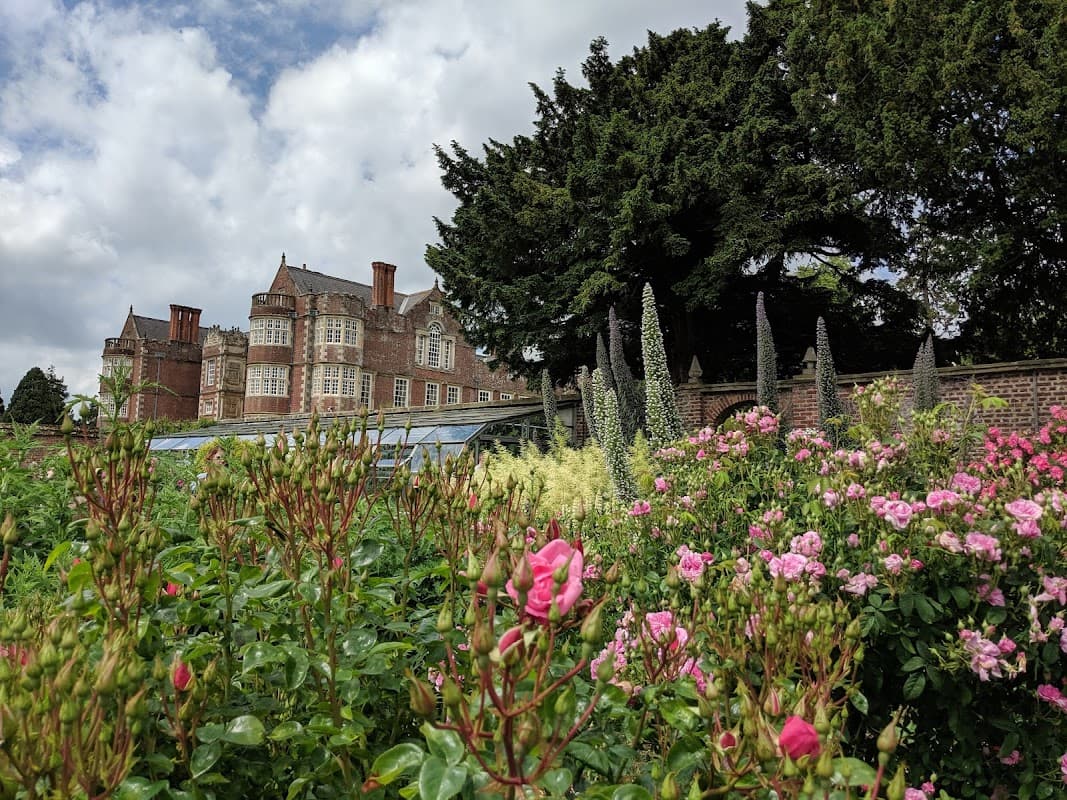 Burton Agnes Hall with lush gardens and blooming flowers in the foreground, under a partly cloudy sky.
