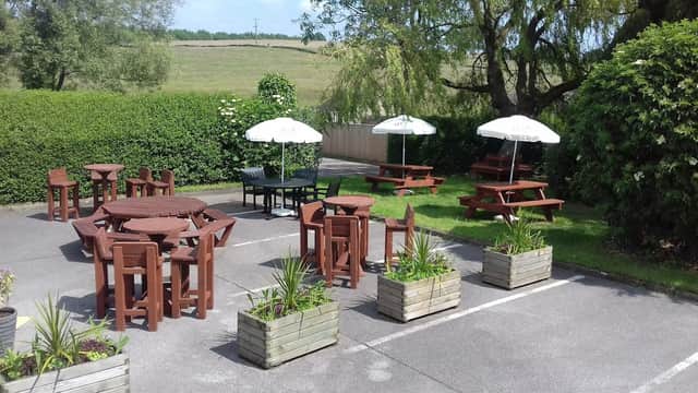 Outdoor seating area with wooden tables, umbrellas, and planters, surrounded by greenery at The Foresters Arms.