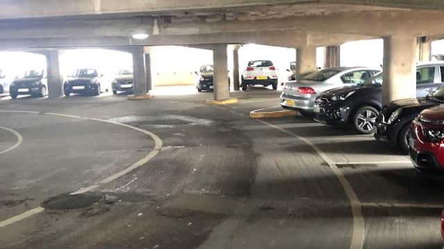 Multi-storey car park interior with parked cars and concrete pillars, featuring a winding driving path.