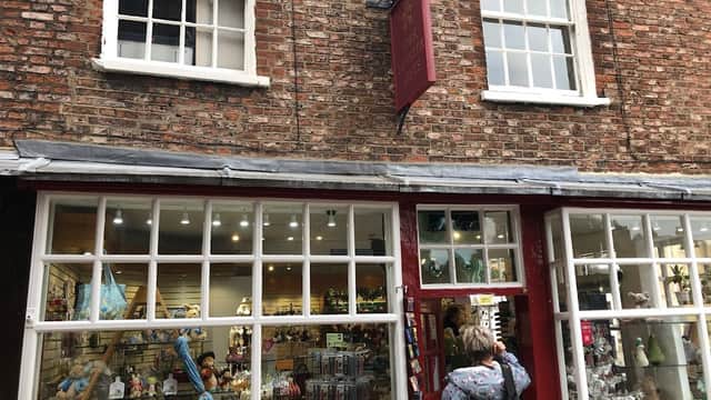 Gift shop with a red storefront, large windows displaying various souvenirs, and a brick wall backdrop.