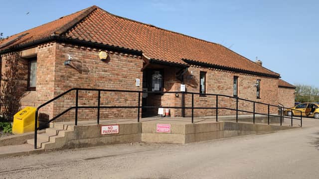 Brick building with a red tiled roof, ramp entrance, and a sign indicating no parking. A taxi is parked nearby.