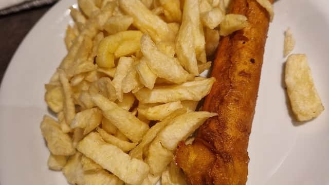 Plate of golden, crispy chips with a single battered fish fillet, served at Fish & Chippery in Skipsea, Yorkshire.