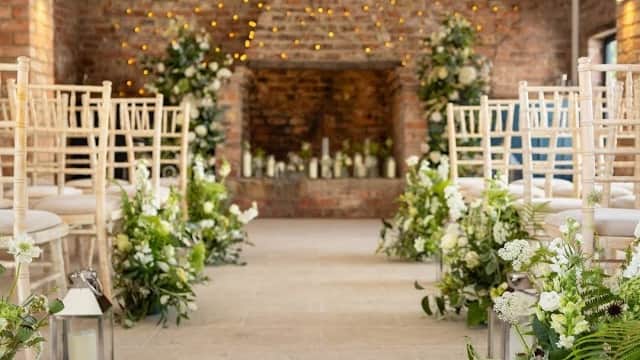 Rustic wedding venue with wooden beams, fairy lights, floral arrangements, and elegant chairs along a stone pathway.