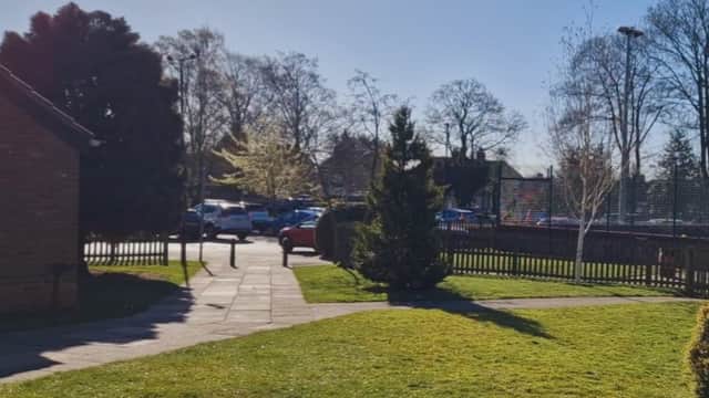 Sunny car park at Galtres Centre, surrounded by trees and grass, with parked cars and a clear blue sky.