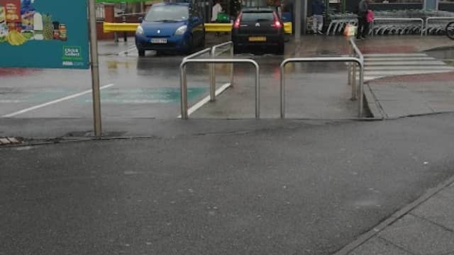 Asda supermarket entrance with green signage, cars parked in front, and shopping trolleys nearby on a cloudy day.
