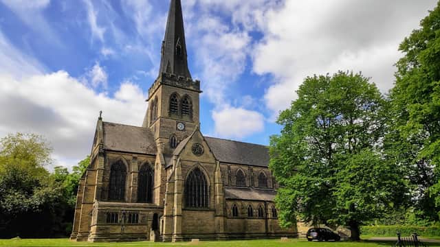 Holy Trinity Church with a tall spire, surrounded by lush greenery and a cloudy blue sky in Wentworth, Yorkshire.