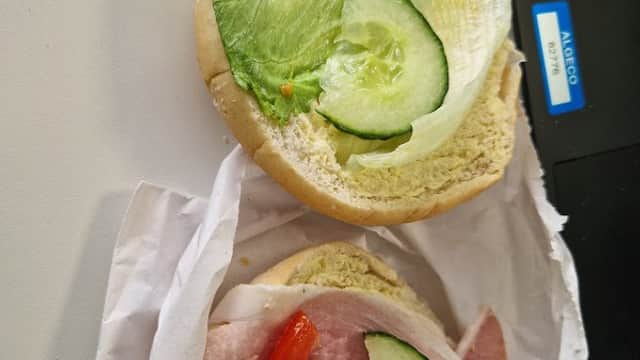 A sandwich bun topped with lettuce, cucumber, and sliced ham with tomatoes, resting on crumpled white paper.