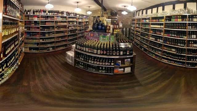 A cozy off-licence with wooden floors, shelves filled with various bottles of beer and spirits, and warm lighting.
