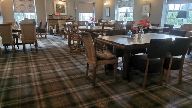 Cozy pub interior with wooden tables, wicker chairs, and a checkered carpet, adorned with floral centerpieces.