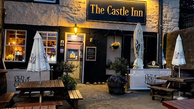The Castle Inn, a charming bar with outdoor seating, illuminated sign, and flower pots, set in a quaint Yorkshire village.