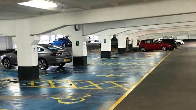 Empty car park with marked spaces, concrete pillars, and parked cars under bright overhead lighting.