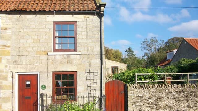 Charming stone cottage with red door, window, and a garden, set against a blue sky in Gillamoor, Yorkshire.