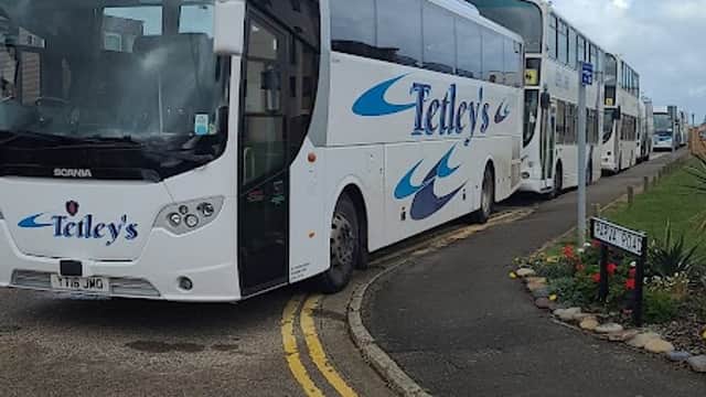 Two white coaches with "Tetley's" branding parked in a coach drop-off area, with a cloudy sky in the background.