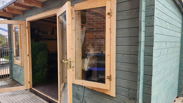 Quaint wooden florist shop with large glass doors and a green exterior, surrounded by potted plants and a welcoming entrance.