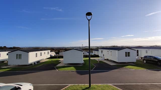 White holiday caravans lined along a paved road, with green grass and a clear blue sky in the background.